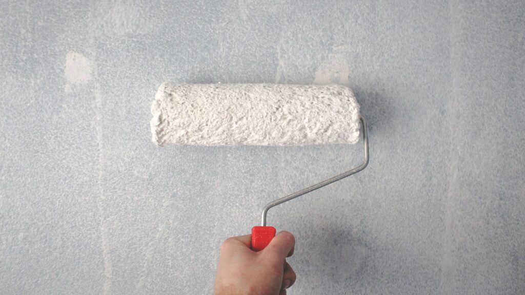 Person using a paint roller applying white paint on a wall representing professional house painting in Avon CT.