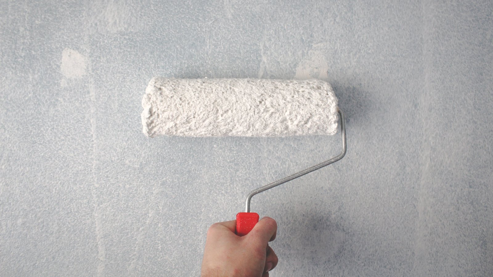 Person using a paint roller applying white paint on a wall representing professional house painting in Avon CT.