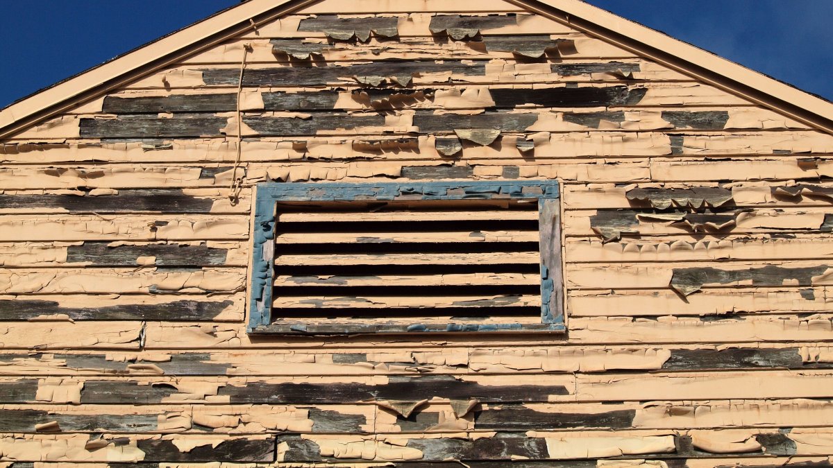 Old wooden house facade with peeling paint against blue sky