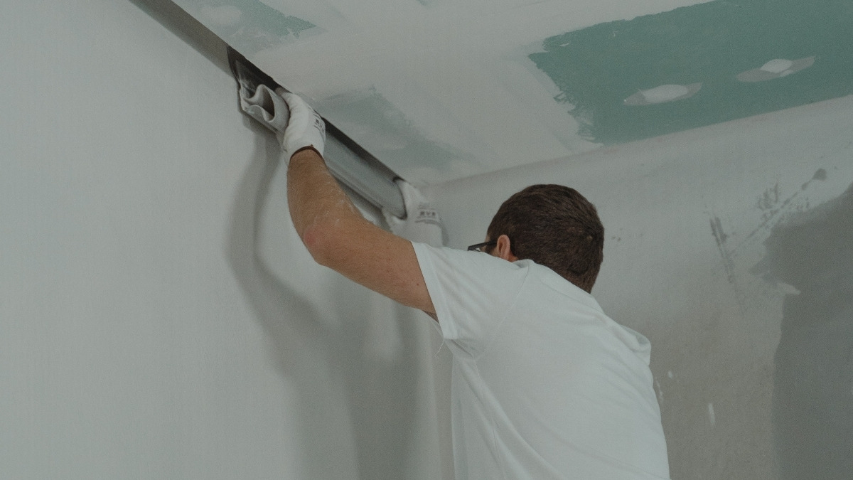 worker using a hand tool to apply joint compound